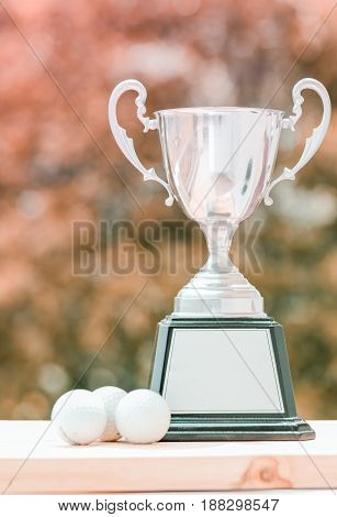 award trophy cup and golf ball on wood in morning orange blur background Winner concept