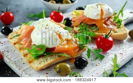 Poached egg on grilled toast with smoked salmon, rucola, olives and vegetables on white board. healthy breakfast.