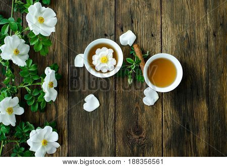 Cup Of Hot Tea With Rosehip And Blooming Flowers On Old Rustic Wooden Background