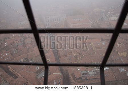 Typical red roofs of Bologna. View from a narrow window with iron grid of Asinelli Tower. Emilia Romagna Italy.
