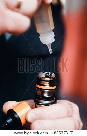 Close-up man is filling an electronic cigarette with a fragrant liquid on a fleece. The spiral is hot. The concept of replacement of cigarettes with tobacco, harmless smoking.