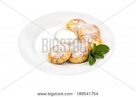 cheese pancakes sprinkled with powdered sugaron on a white plate with sour cream decorated with mint leaves on a white background