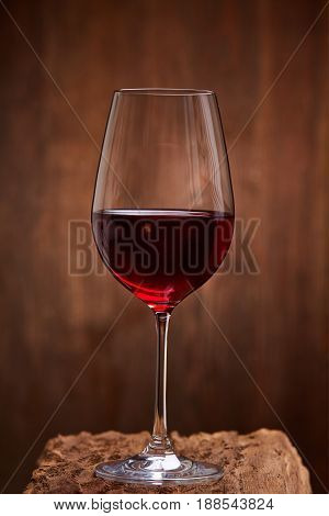 Close-up of crystal half-ful wineglass with red wine standing on wooden stand against wooden background. Luxury lifestyle, celebration and relexation. Natural material and product. Sommelier and tasting. Horizontal photo.