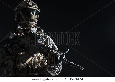 Army soldier in Protective Combat Uniform holding Special Operations Forces Combat Assault Rifle. Studio shot, dark contrast, cropped, black dark background