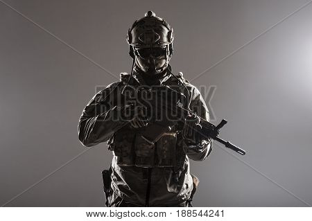 Army soldier in Protective Combat Uniform holding Special Operations Forces Combat Assault Rifle. Studio shot, low key, cropped, black dark background, contour shot