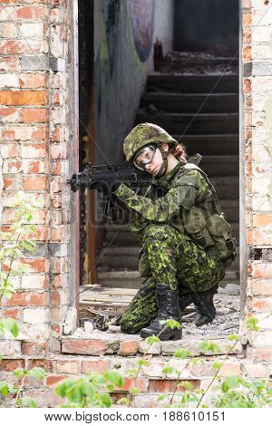 Portrait of armed woman with camouflage. Young female soldier observe with firearm. Child soldier with gun in war hearth house ruins background. Military army people concept