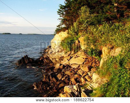 Casco bay Maine's rocky shoreline with the sun shining on the rocks.
