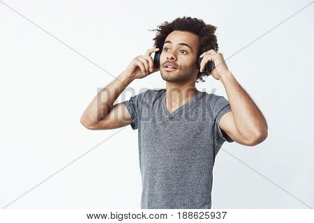 Young handsome african man listening to music in headphones over white background. Copy space.