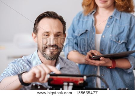 Lets start. Cheerful delighted handsome man smiling and pressing a button while doing 3d printing