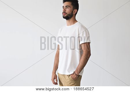 Serius bearded male looks ahead with thinking face expression wears white simple blank t-shirt isolated on mockup ready for design