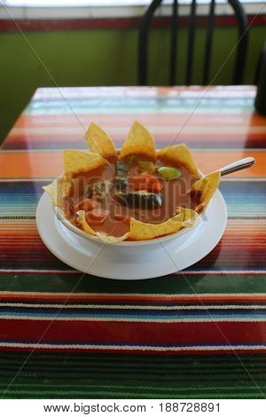 Chips and Salsa. Fresh Deep Fried Corn Chips and Fresh Tomato Salsa in a yellow plastic basket with a paper lining on a stripped colored cloth table cloth.  