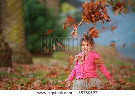 outdoor portrait of young happy child girl playing with autumn leaves in park on natural background