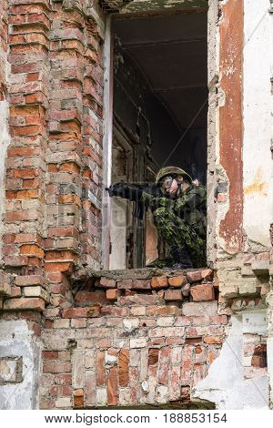 Portrait of armed woman with camouflage. Young female soldier observe with firearm. Child soldier with gun in war hearth house ruins background. Military army people concept