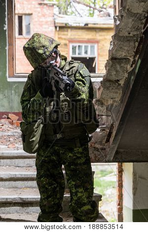 Portrait of armed woman with camouflage. Young female soldier observe with firearm. Child soldier with gun in war hearth house ruins background. Military army people concept