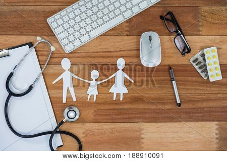 Paper cut out family chain with medicines, mouse, keyboard, stethoscope, clipboard and spectacles on table