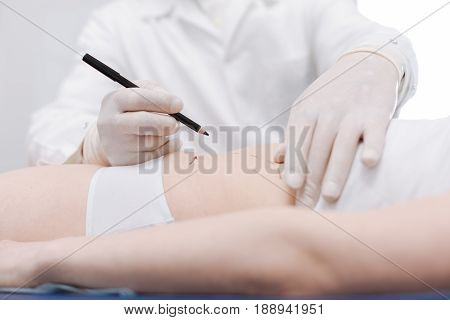 Working on perfect shape. Proficient hardworking scrupulous doctor preparing his patient for upcoming cosmetic procedure while drawing the guidelines on her belly