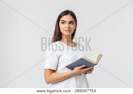 Portrait of a beautiful young woman casualy dressed standing isolated over white background, reading a book