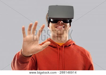 3d technology, virtual reality, entertainment and people concept - happy young man in vr glasses playing game and touching something imaginary over grey background