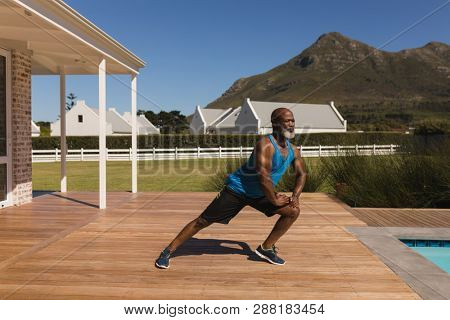 Front view of an active senior African American man performing stretching exorcise in the backyard of home