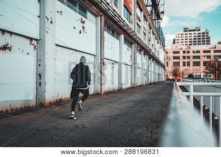 Back View Of Runner Training In City Port. Man Athlete Running Throug Hurban Gateway