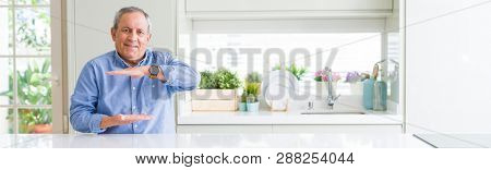 Wide angle perspective of handsome senior man at home gesturing with hands showing big and large size sign, measure symbol. Smiling looking at the camera. Measuring concept.