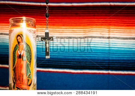 Wood And Silver Crucifix With Virgin Mary Prayer Candle To The Left, With Mexican Blanket As Backdro