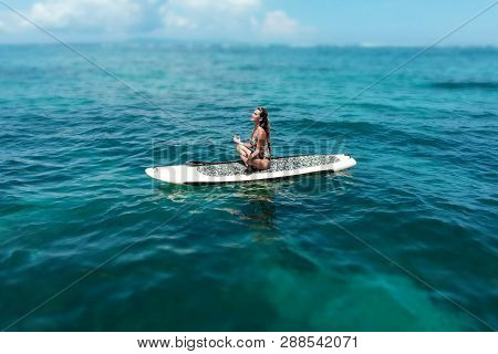 Young Beautiful Woman Meditating In A Sea At Sup Paddleboarding. Healthy Lifestyle. Girl In Yoga Pos