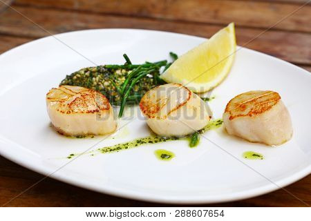 Close Up Portion Of Three Grilled Scallops On White Plate Over Brown Wooden Table, High Angle View
