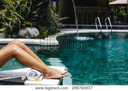 Woman relaxing in swimming pool in Bali luxury resort. Foot spa and skin care lifestyle photo.