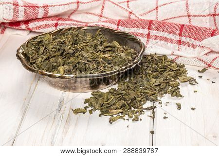 Lot Of Pieces Of Dry Green Tea In Old Iron Bowl On White Wood