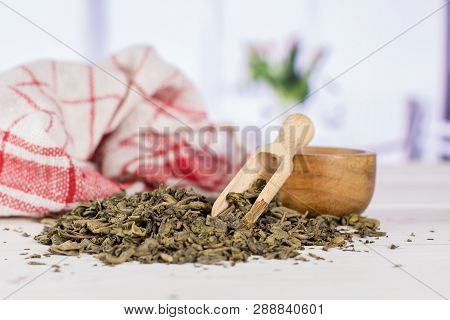 Composition Lot Of Pieces Of Dry Green Tea With Wooden Scoop With Red Flowers In White Kitchen