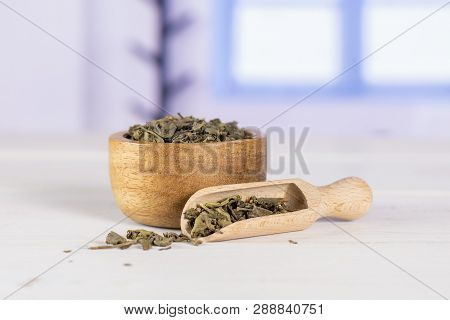 Lot Of Pieces Of Dry Green Tea In A Scoop With Wooden Bowl With Blue Window