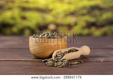 Lot Of Pieces Of Dry Green Tea In A Scoop With Wooden Bowl In A Forest