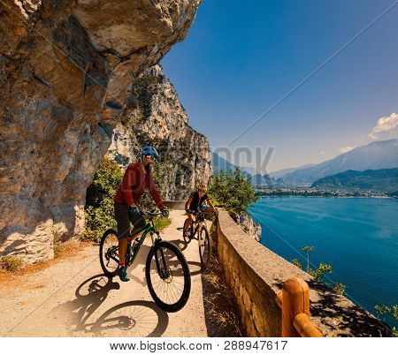 Cycling woman and man riding on bikes at sunrise mountains and Garda lake landscape. Couple cycling MTB enduro flow sentiero ponale trail track. Outdoor sport activity.