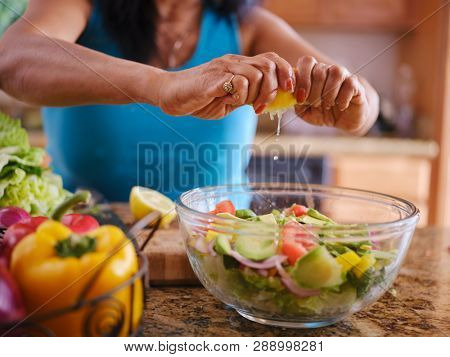 elderly thai woman sqeezing lemon juice into salad bowl