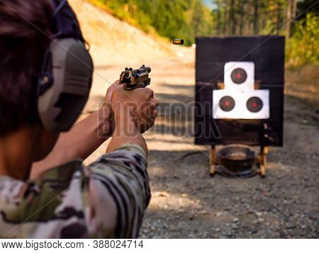 A Young Man Target Practicing With His Pistol. The Spent Casing Is Frozen In Midair. Notice The Fron