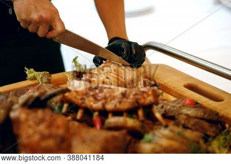 A Cook In A Restaurant Cuts Meat Cooked On Fire, A Huge Assorted Meat For A Large Company, A Place F