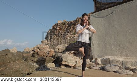 Young Woman Practising Yoga On Sunny Day On The Rocky Sea Coast.tree Posture. High Quality Photo