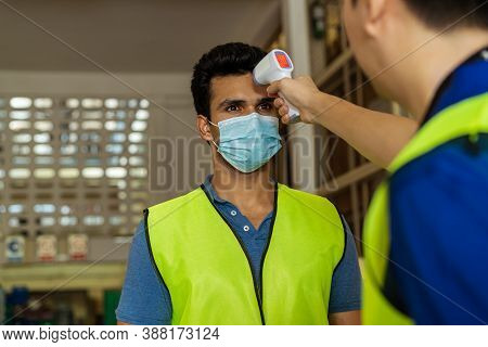 Young Indian Factory Warehouse Worker Wearing Face Mask Getting Body Temperature Check With Infrared