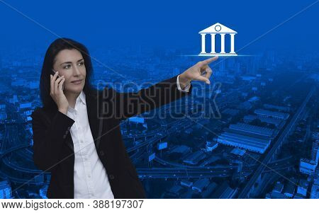 Caucasian Businesswoman Talking On Her Cell Phone And Pointing To Bank Flat Icon Over Modern City To