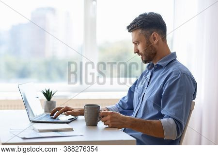 Remote Work. Handsome Male Freelancer Using Laptop And Drinking Coffee, Working Remotely At Home Off