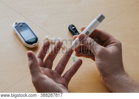 Close Up Of A Man's Hand Using A Lancet On His Finger To Check Blood Sugar Using A Glucose Meter, Us