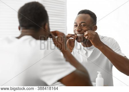 Black Man Cleaning Teeth With Floss Standing Near Mirror In Bathroom At Home In The Morning. Healthy