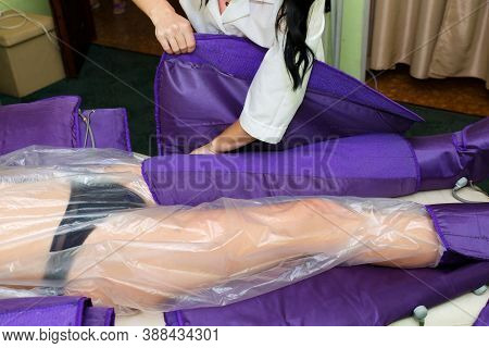The Beautician Of The Spa Salon Covers The Legs Of A Woman In A Special Suit For Pressotherapy.