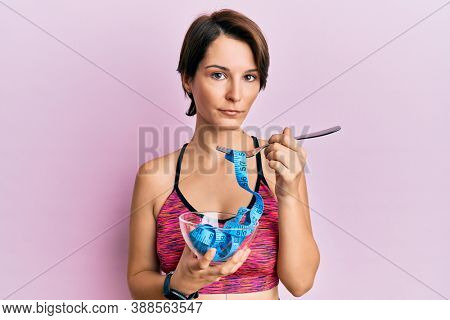 Young brunette woman with short hair eating measure meter doing diet for weight loss relaxed with serious expression on face. simple and natural looking at the camera. 
