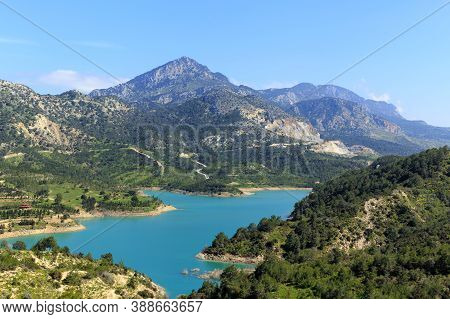 Reservoir At The Foot Of High Mountains. Green Mountains And Blue Water In The Reservoir.