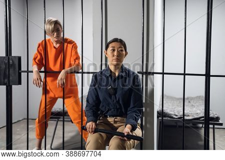 A Young Taskmaster In Uniform Sits On A Chair Next To The Camera Of A Blonde Criminal.