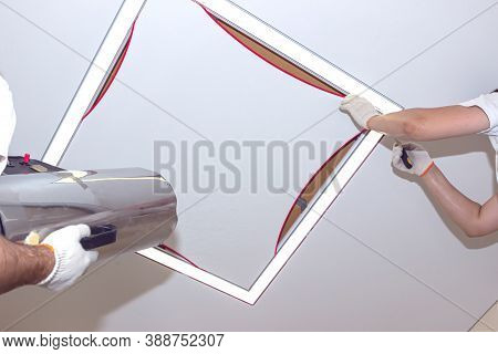 Repairmen Stretch A White Ceiling In A Room. Workers Use A Heat Gun To Install A Stretching Ceiling.