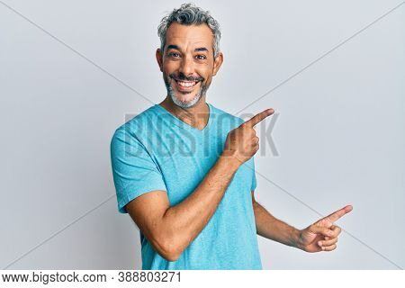 Middle age grey-haired man wearing casual clothes smiling and looking at the camera pointing with two hands and fingers to the side. 