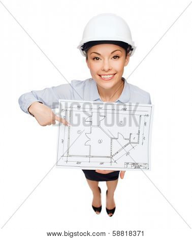 building, developing, consrtuction and architecture concept - smiling businesswoman in white helmet pointing finger to blueprint
